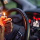 A woman lights a cigarette behind the wheel of her car.